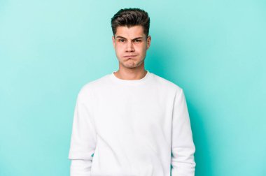 Mavi arka planda izole edilmiş genç beyaz adamın yanakları şişer, yorgun bir ifadesi vardır. Yüz ifadesi kavramı.