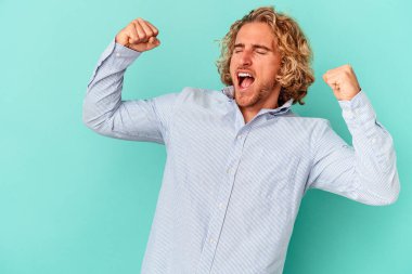 Mavi arka planda izole edilmiş genç beyaz bir adam zaferden sonra yumruğunu kaldırıyor, kazanan konsept..