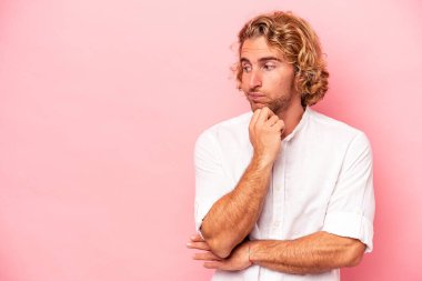 Pembe arka planda izole edilmiş genç beyaz adam rahatlamış bir şeyin fotokopi odasına baktığını düşünüyor..