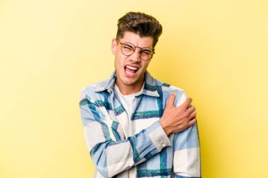 Sarı arka planda izole edilmiş, omuz ağrısı olan genç beyaz bir adam..