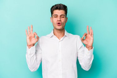 Mavi arka planda izole edilmiş genç beyaz adam yorucu bir günün ardından rahatlıyor. Yoga yapıyor..