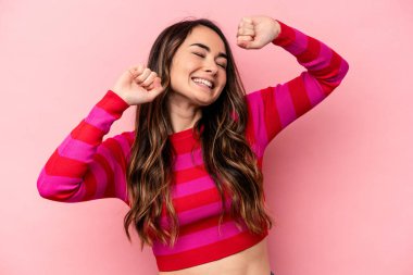 Pembe arka planda soyutlanmış genç beyaz bir kadın özel bir günü kutluyor, atlıyor ve enerjiyle kollarını kaldırıyor..