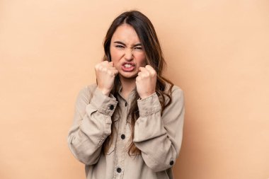 Beyazlı genç bir kadın bej arka planda izole edilmiş, yumruğunu kameraya gösteriyor, agresif yüz ifadesi var..