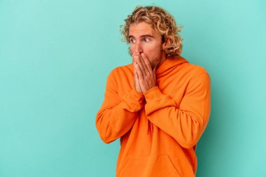 Kafkasyalı genç adam mavi arka planda izole edilmiş. Düşünceli bir şekilde ağzıyla ağzını kapatan bir fotokopi odasına bakıyor..