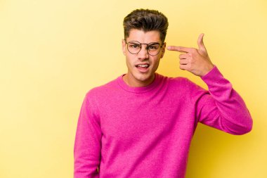 Sarı arka planda izole edilmiş genç beyaz adam işaret parmağıyla hayal kırıklığı jesti yapıyor..