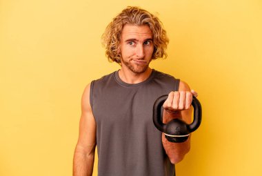Sarı arka planda halter kaldıran genç sporcu, kafası karışmış ve kendinden emin değil..