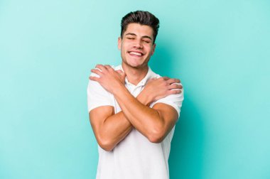 Kafkasyalı genç adam mavi arka planda izole edilmiş, güler yüzlü ve mutlu..