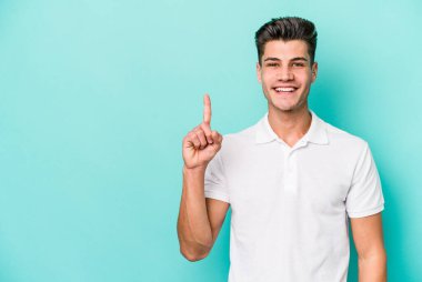 Mavi arka planda izole edilmiş genç beyaz adam bir numarayı parmağıyla gösteriyor..