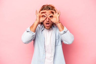 Pembe arka planda izole edilmiş genç beyaz adam bir başarı fırsatı bulmak için gözlerini açık tutuyor..