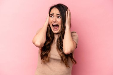 Pembe arka planda izole edilmiş genç, beyaz bir kadın. Kulakları kulaklarıyla kapatıyor. Çok fazla ses duymamaya çalışıyor..