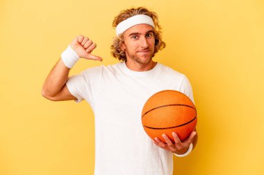 Sarı arka planda izole edilmiş genç basketbolcu beyaz adam gururlu ve kendinden emin hissediyor, örnek olarak..