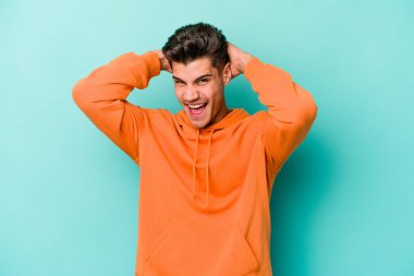 Genç beyaz adam mavi arka planda izole edilmiş bağırıyor, çok heyecanlı, tutkulu, bir şeyden memnun..