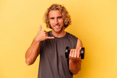 Sarı arka planda halter yapan genç sporcu parmaklarıyla bir cep telefonu hareketi gösteriyor..