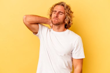 Genç beyaz adam sarı arka planda izole edilmiş dirsek masajı yapıyor, kötü bir hareketin ardından acı çekiyor..