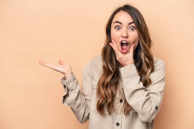 Bej arka planda izole edilmiş beyaz bir kadın avuç içinde fotokopi alanı tutuyor, el üstünde tutuyor. Şaşırmış ve mutlu..