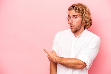 Pembe arka planda izole edilmiş genç beyaz adam gülümsüyor ve boş alanda bir şeyler gösteriyor..