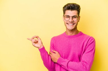 Sarı arka planda izole edilmiş genç beyaz adam işaret parmağıyla işaret ederek gülümsüyor..