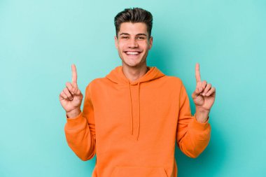 Mavi arka planda izole genç beyaz adam işaret iki ön parmakları boş bir boşluk gösteren.
