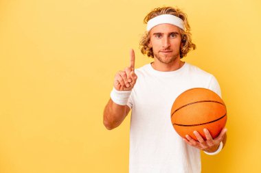 Genç basketbolcu beyaz adam sarı arka planda izole edildi. Parmak iziyle bir numarayı gösteriyor..