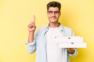 Sarı arka planda izole edilmiş pizzaları tutan beyaz bir adam bir numarayı parmağıyla gösteriyor..