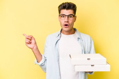 Sarı arka planda izole edilmiş pizzalar tutan genç beyaz adam...