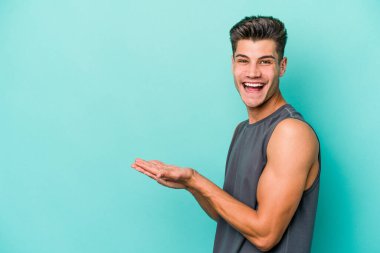 Mavi arka planda izole edilmiş genç beyaz bir adam palmiyesinde bir kopya alanı tutuyor..