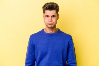 Sarı arka planda izole edilmiş genç beyaz adam yanakları patlatır, yorgun bir ifadeye sahiptir. Yüz ifadesi kavramı.