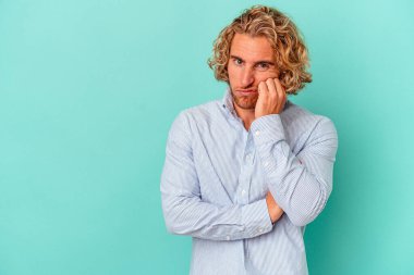 Mavi arka planda izole edilmiş, üzgün ve dalgın hisseden, kopyalama alanına bakan genç beyaz bir adam..