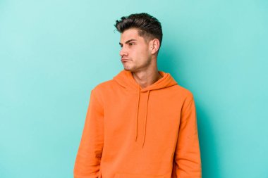 Mavi arka planda izole edilmiş genç beyaz adam omuzlarını silkeliyor ve gözleri açık..