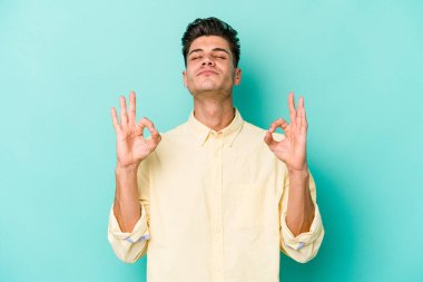 Mavi arka planda izole edilmiş genç beyaz adam yorucu bir günün ardından rahatlıyor. Yoga yapıyor..