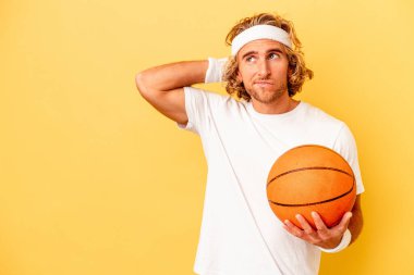Young basketball player caucasian man isolated on yellow background touching back of head, thinking and making a choice.