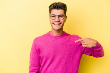 Sarı arka planda izole edilmiş genç beyaz bir adam gömlek fotokopi alanını elle gösteriyor, gururlu ve kendinden emin.