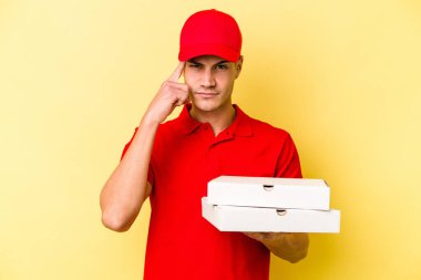 Sarı arka planda pizza tutan beyaz bir adam şakağı parmağıyla işaret ediyor, düşünüyor ve bir göreve odaklanıyor..