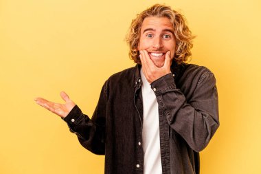 Sarı arka planda izole edilmiş genç beyaz bir adam bir avuç içinde fotokopi alanı tutuyor, el üstünde tutuyor. Şaşırmış ve mutlu..