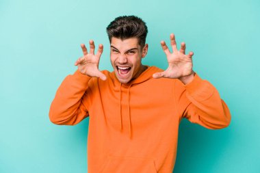 Mavi arka planda izole edilmiş genç beyaz adam pençelerini kedi taklidi yaparken gösteriyor, agresif bir hareket..