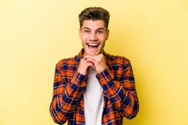 Kafkasyalı genç adam sarı arka planda izole edilmiş şans için dua ediyor, şaşırmış ve ağzını açıp önüne bakıyor..