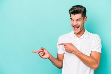 Mavi arka planda izole edilmiş genç beyaz adam işaret parmağıyla fotokopi alanını işaret ederek heyecan ve arzusunu ifade ediyor..