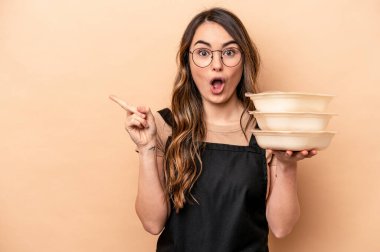 Beyaz tenli genç bir kadın bej arka planda saklanmış plastik kaplar taşıyor.