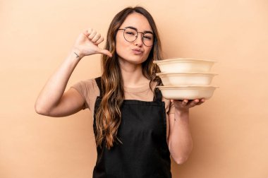 Beyaz tenli genç bir kadın bej arka planda saklanmış plastik kaplar taşıyor. Gururlu ve kendinden emin, örnek olarak..