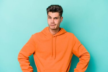 Kafkasyalı genç adam mavi arka planda izole edilmiş üzgün, ciddi yüzlü, mutsuz ve hoşnutsuz..