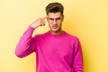Sarı arka planda izole edilmiş genç beyaz bir adam şakağı parmağıyla işaret ediyor, düşünüyor ve bir göreve odaklanıyor..