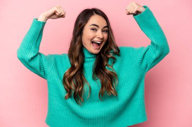 Pembe arka planda izole edilmiş genç beyaz kadın güçlü bir hareket gösteriyor. Kollarıyla, kadınsı gücün sembolü.