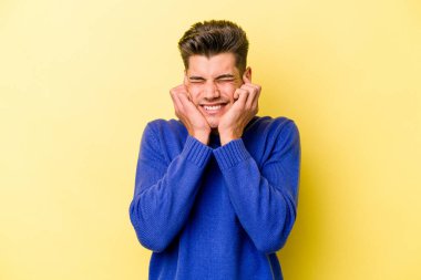 Sarı arka planda izole edilmiş genç beyaz adam elleriyle kulakları örtüyor..