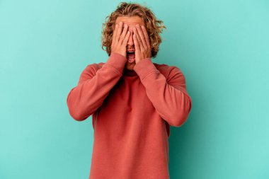 Mavi arka planda izole edilmiş genç beyaz adam yüzünün yarısını palmiye ile kaplayarak eğleniyor..