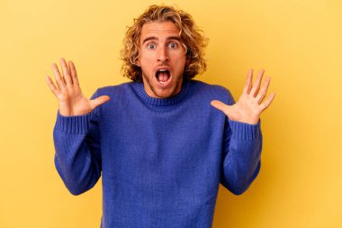 Sarı arka planda izole edilmiş genç beyaz adam gökyüzüne haykırıyor, yukarı bakıyor, hayal kırıklığına uğramış..