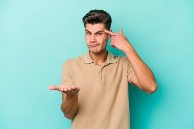 Kafkasyalı genç adam mavi arka planda izole edilmiş ve elinde bir ürün tutuyor..