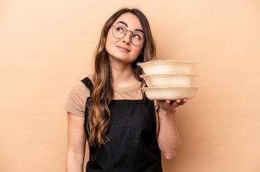 Beyaz tenli genç bir kadın bej arka planda saklanmış vaziyette hedeflerine ve amaçlarına ulaşma hayali kuruyor.