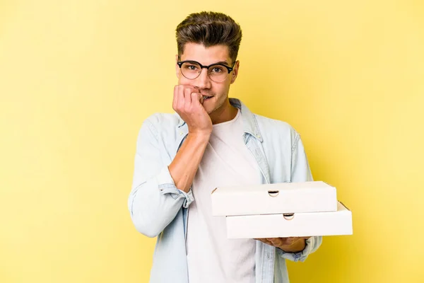 Young Caucasian Man Holding Pizzas Isolated Yellow Background Biting Fingernails — Fotografia de Stock