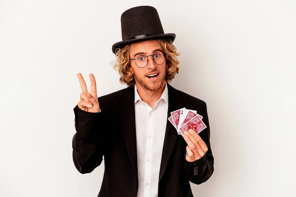 若い魔術師の白人の背景に孤立した魔法のカードを保持する白人男性喜びと屈託のない指で平和のシンボルを示す — ストック写真