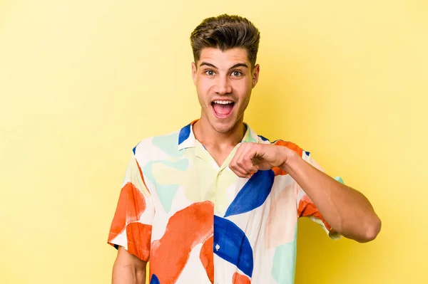 Young caucasian man isolated on yellow background surprised pointing with finger, smiling broadly.